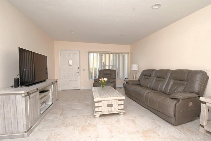 Living room with a view of the front door area. New ceramic tile flooring installed in 2022. Recessed lighting in the ceiling. Popcorn ceiling has been removed.