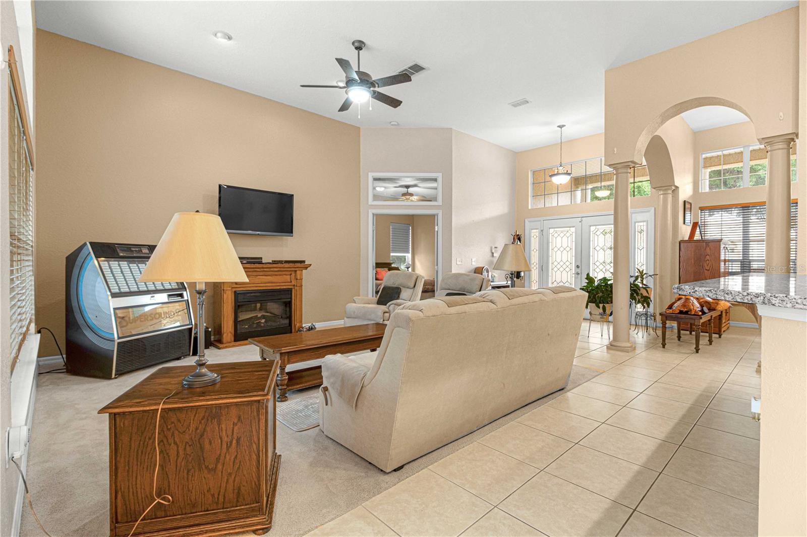 Open living room area, carpet, high ceiling, natural lighting.