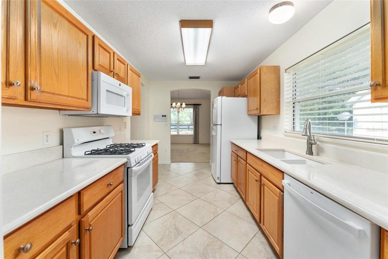 KITCHEN with GALLEY DESIGN features OAK CABINETS with PULL OUTS, SOLID SURFACE COUNTERTOPS, newer white appliances.
