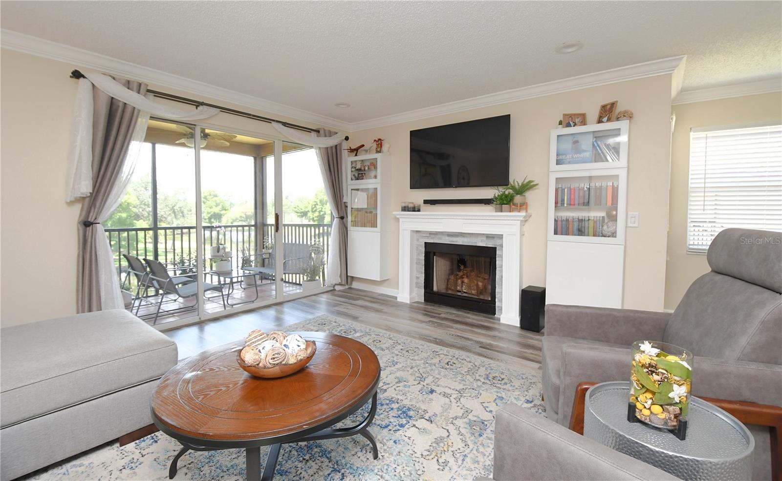 Living room with a gorgeous view of the gulf course and a beautiful pond. The room features luxury vinyl flooring, crown molding and a beautiful wood burning fire place.