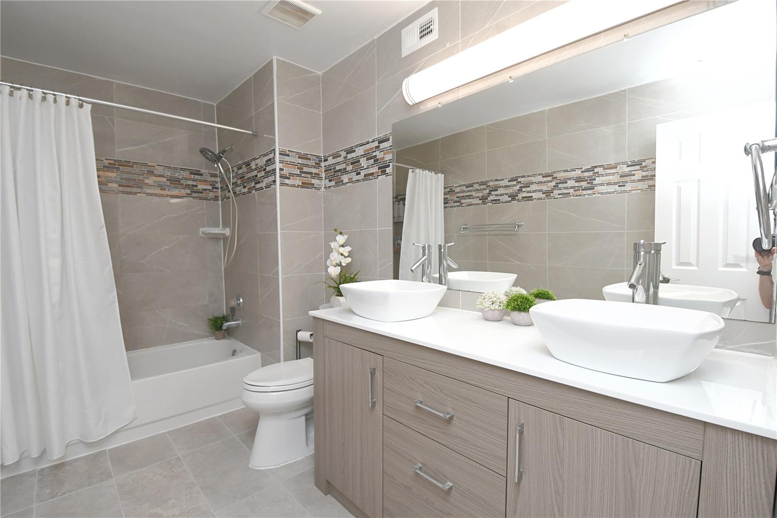 Master bathroom features a low/easy accessible bathtub, sleek tiles, double vanity with modern vessel sinks and contemporary lighting.
