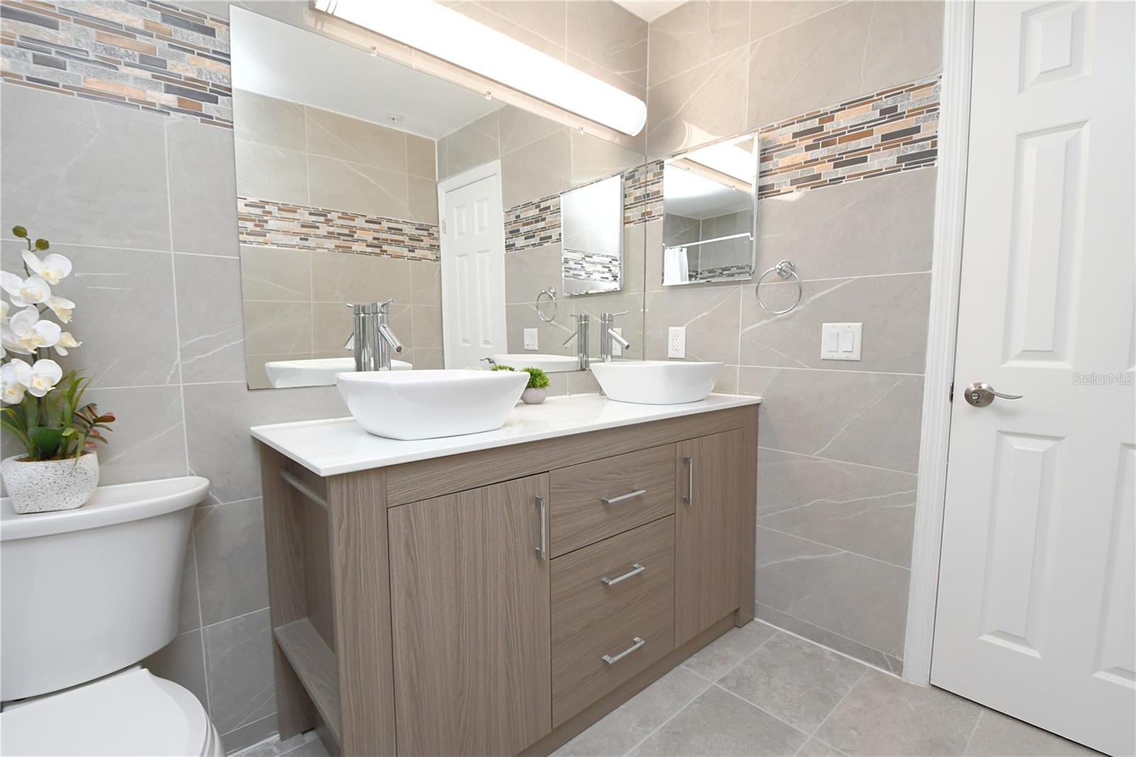 Master bathroom features sleek tiles, double vanity with modern double vessel sinks and contemporary lighting.