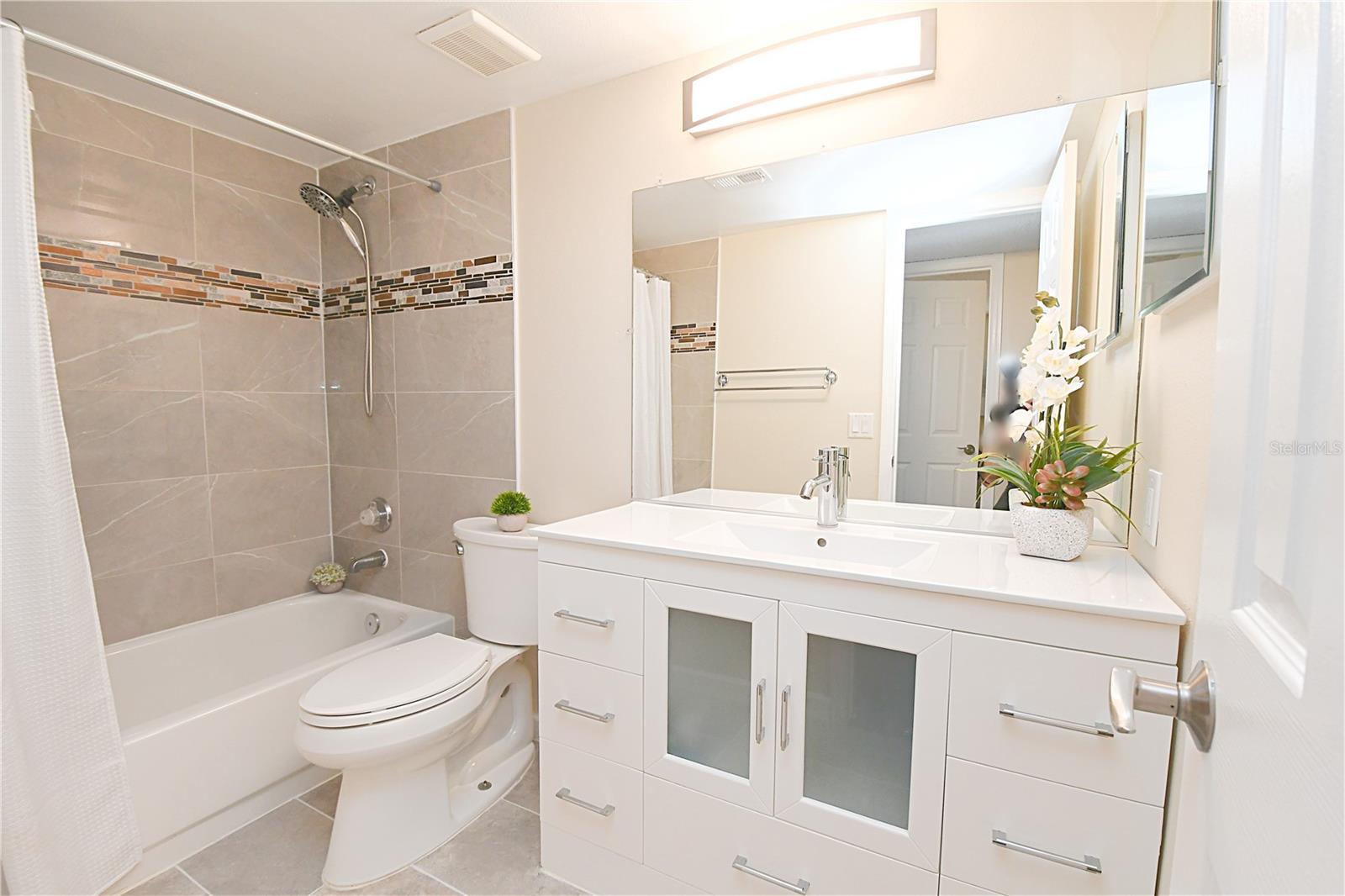Bathroom #2 features an easy accessible bathtub, sleek tiles, modern vanity, large mirror and contemporary lighting.