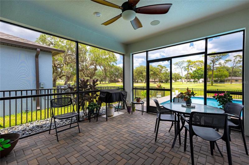 Oversized screen room with pavers and ceiling fan lead to the beautiful pool area.