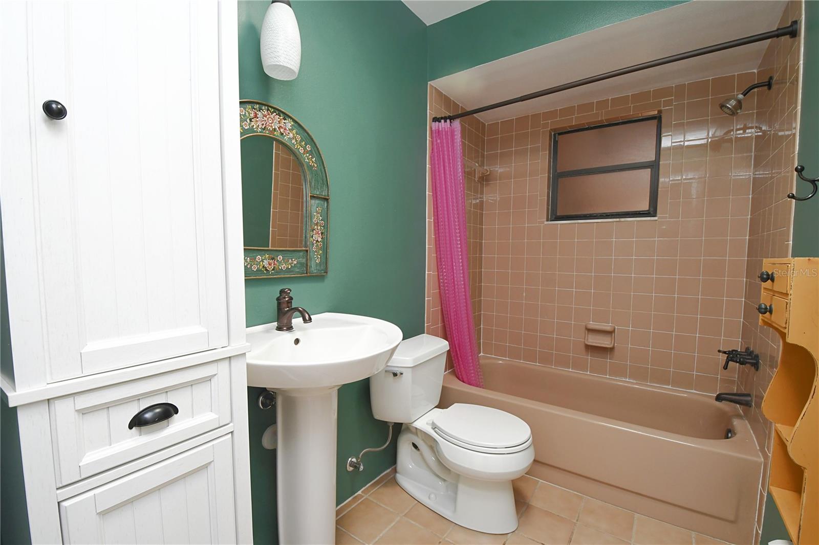 The bathroom features ceramic tile flooring, a tub with shower, a pedestal sink and a skylight.
