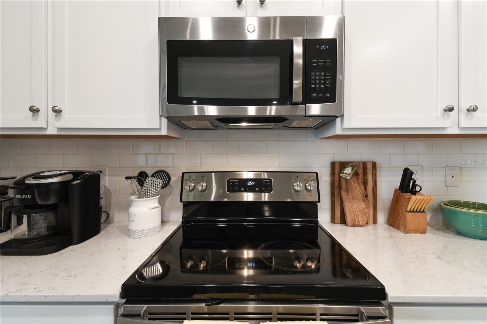 White subway tile backsplash, black/stainless electric stove and microwave with exhaust fan.