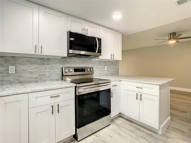 The Well-equipped Kitchen with upgraded LG stainless-steel appliances, including a convection oven with air fryer, soft close cabinets, designer marble countertops extended for a convenient breakfast bar, a stylish glass tile backsplash, an upgraded Kohler faucet, can lighting, and a spacious pantry