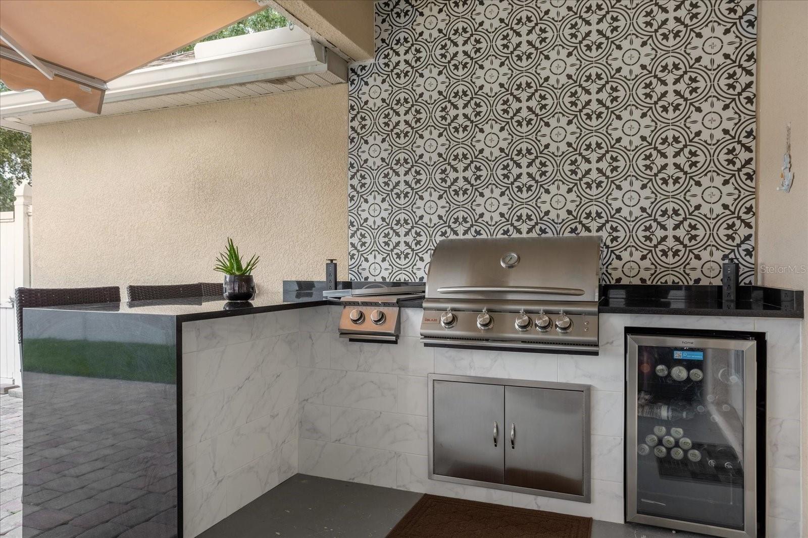High-end summer kitchen with grill, side burner, fridge, and waterfall quartz countertop