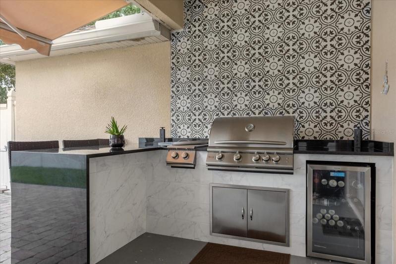High-end summer kitchen with grill, side burner, fridge, and waterfall quartz countertop