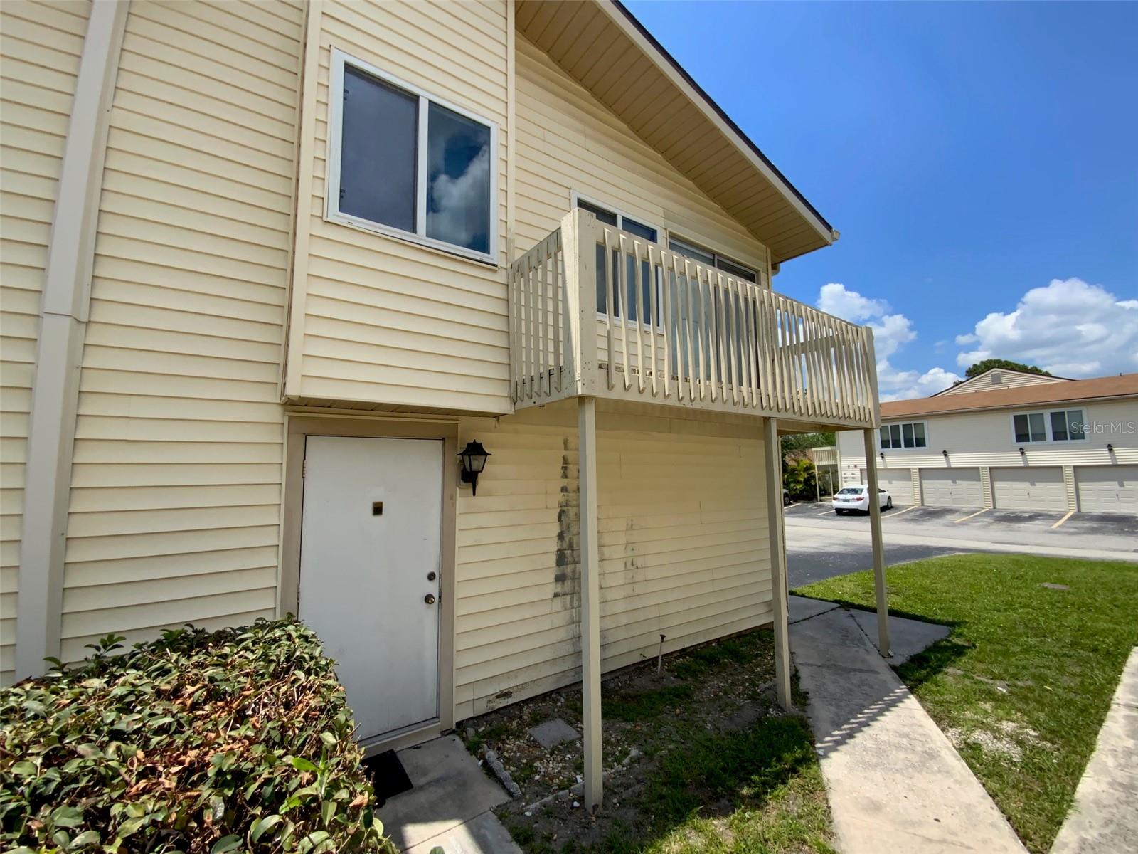 Unit entrance, balcony and sidewalk to garage and driveway