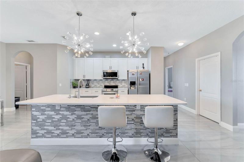 Follow the natural flow into the gorgeous kitchen; glowing like it was ripped from the pages of a home magazine with chic shaker style cabinetry, large island with a glass tile accent wall to match the backsplash, stainless steel appliances and modern pendant lighting over the breakfast bar!