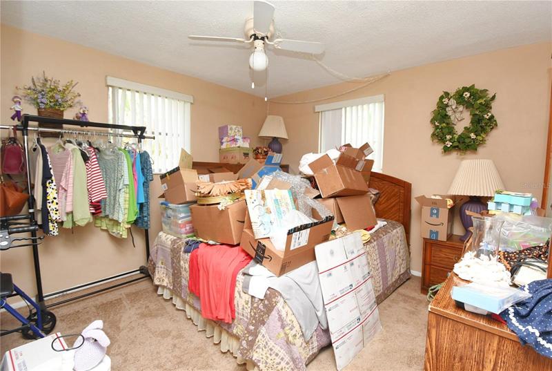 Bedroom 2 is currently "packing central" ... Look beyond the boxes to a large built in closet, plush carpeting, a ceiling fan and two windows with vertical blinds.