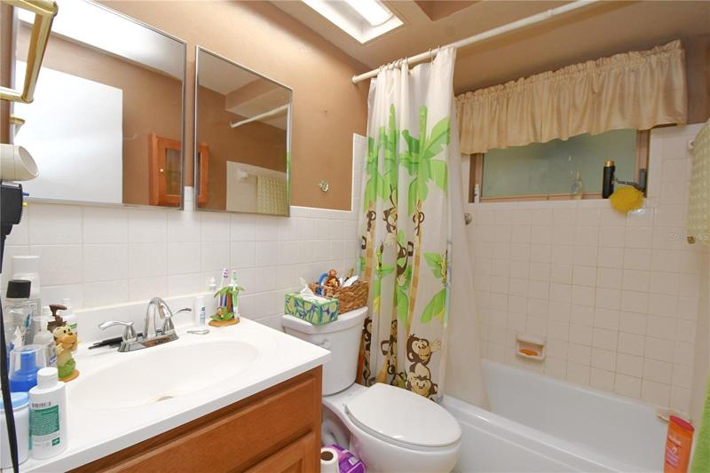 The bathroom features a tub with shower, sink and mirrored vanity with storage and overhead lighting.