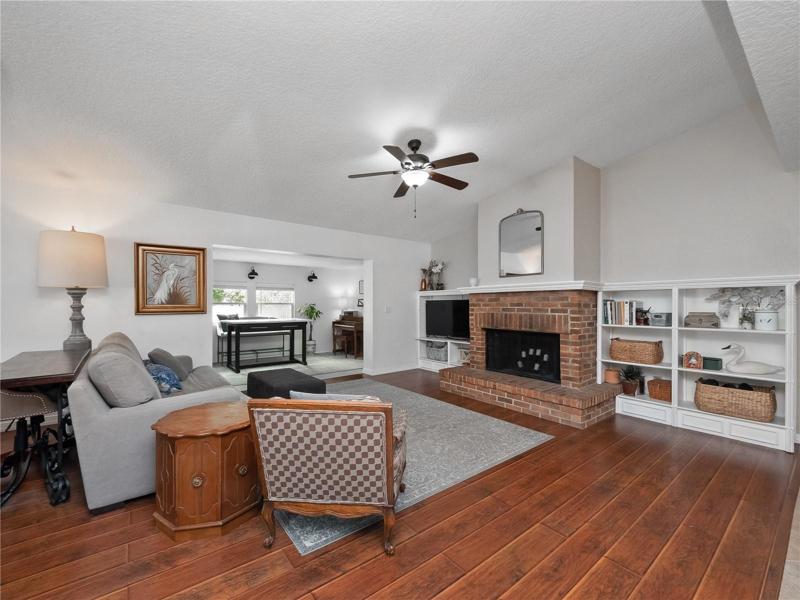 The large living room features dramatic vaulted ceilings, wood floor, wood burning fireplace and built in shelving.
