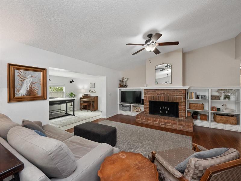The large living room features dramatic vaulted ceilings, wood floor, wood burning fireplace and built in shelving.
