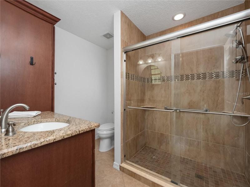 The primary suite has updated flooring, a walk in closet, access to the covered, screened in lanai and large backyard. The primary en-suite bathroom has been updated with solid wood dual sink vanity topped with granite along with a walk in shower.