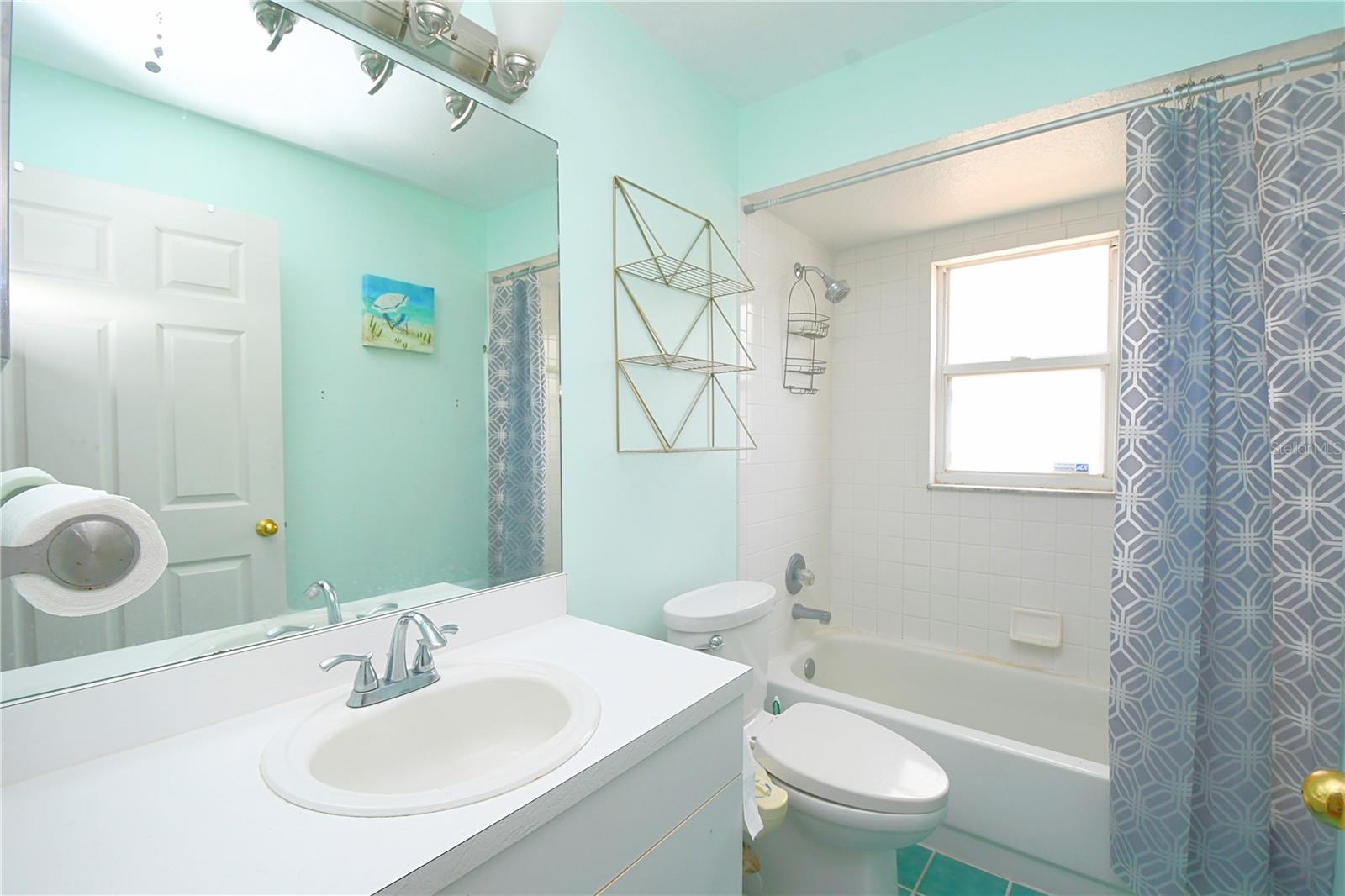 Bathroom two features a tub with shower, a mirrored vanity with storage and up light fixture.