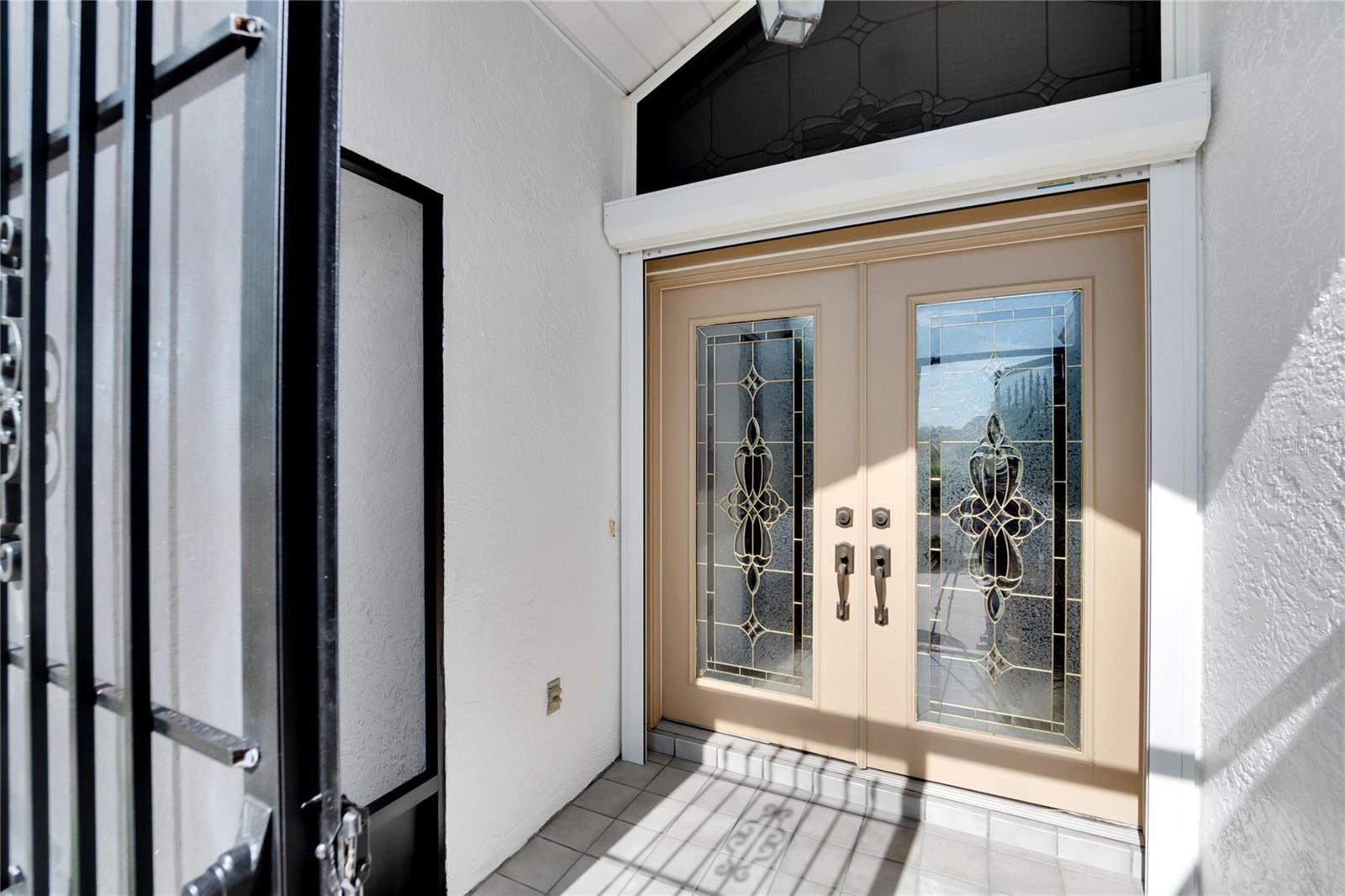 French leaded glass door with leaded glass transom window above.  Transom window has hurricane screen.  Door has hurricane shutters.