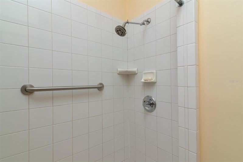 The stall shower has a ceramic tile surround and grab bar.