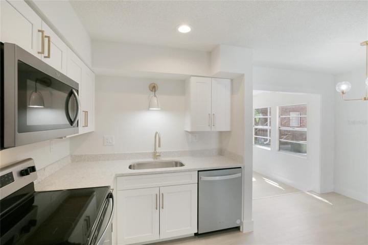 The kitchen boasts stainless steel appliances and sleek quartz countertops, complemented by gold accents in the cabinet pulls and kitchen light fixture for a touch of opulence.