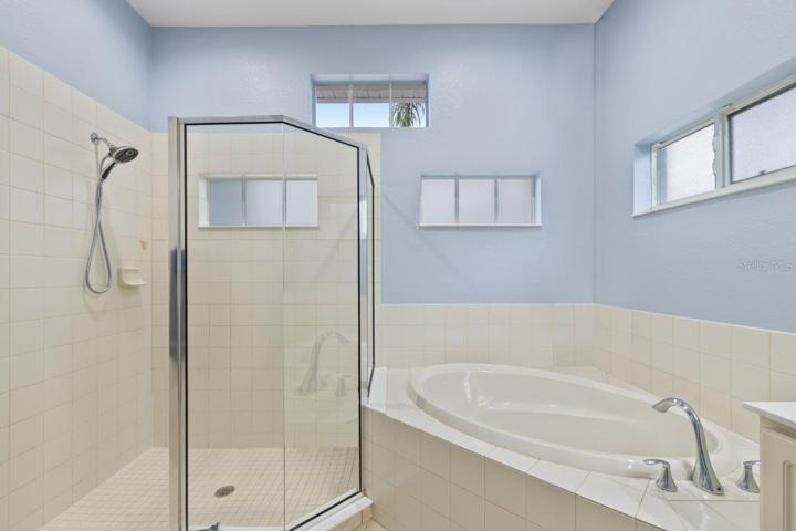 Ensuite owners bathroom featuring a walk-in glassed enclosed shower, garden tub, dual sinks, and two walk in closets.