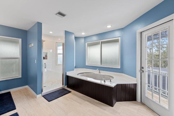 Newly Remodeled Owners ensuite bathroom featuring porcelain tile, dual vanities, a garden tub, glass enclosed shower, and direct access to the wrap around screened-in lanai.