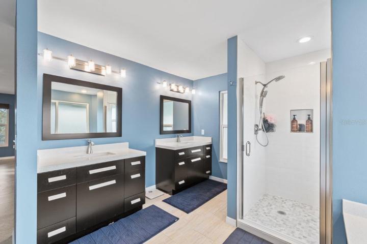 Newly Remodeled Owners ensuite bathroom featuring porcelain tile, dual vanities, a garden tub, glass enclosed shower, and direct access to the wrap around screened-in lanai.