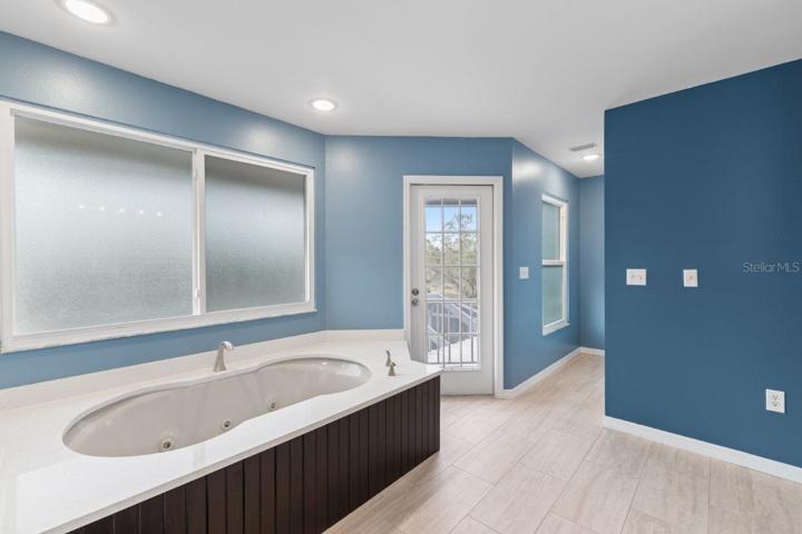Newly Remodeled Owners ensuite bathroom featuring porcelain tile, dual vanities, a garden tub, glass enclosed shower, and direct access to the wrap around screened-in lanai.