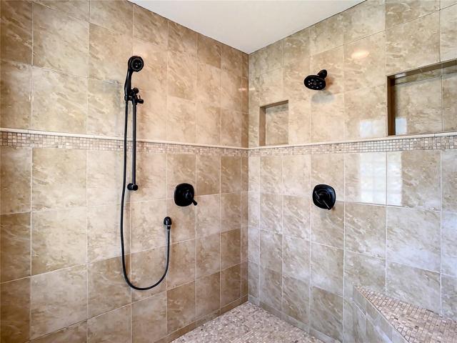 Walk-in tiled shower has multiple shower heads.
