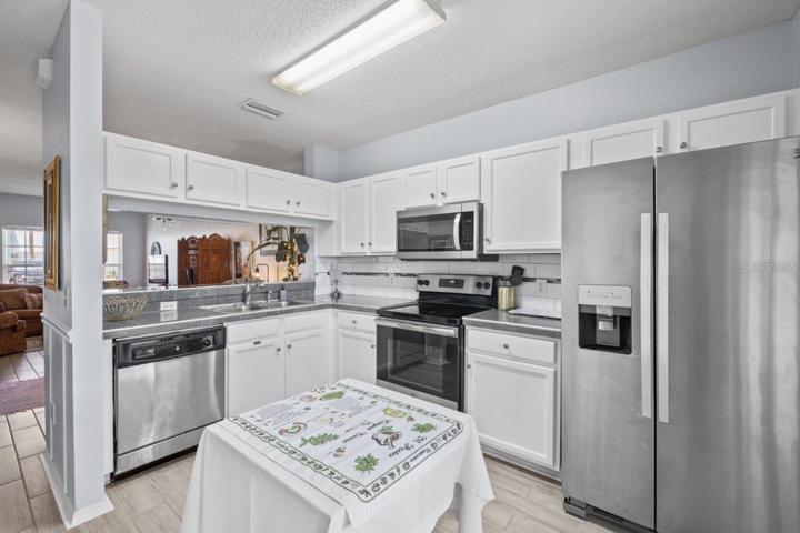 Open Kitchen featuring renovated tile countertops, wood look tile flooring, stainless steel appliances, and direct access to the back lanai