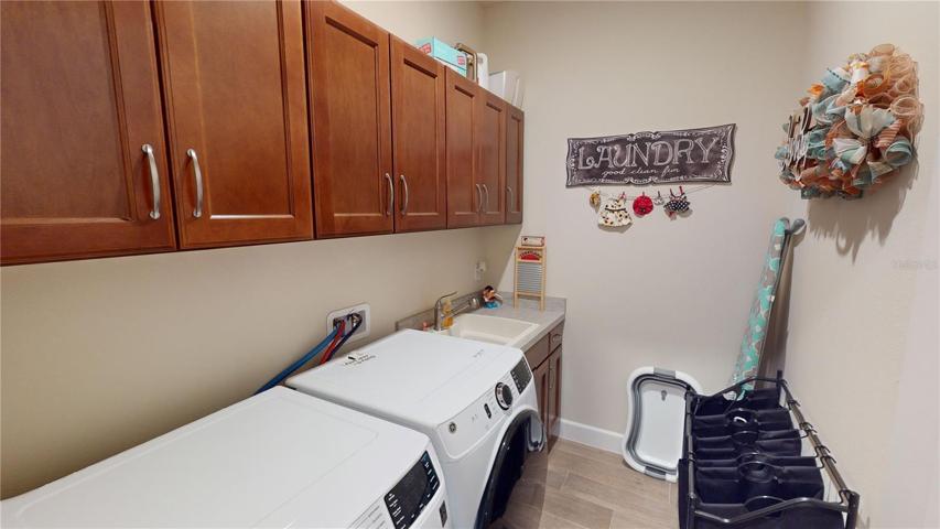 This photo showcases a space that's designed to cater to your daily needs while maintaining a consistent aesthetic with the kitchen. The rich wood cabinetry, harmoniously matching the kitchen's design, adds a touch of continuity throughout your home. The inclusion of a sink enhances functionality, making laundry tasks more convenient and efficient. Discover a space that goes beyond the ordinary, offering both style and purpose in perfect balance.