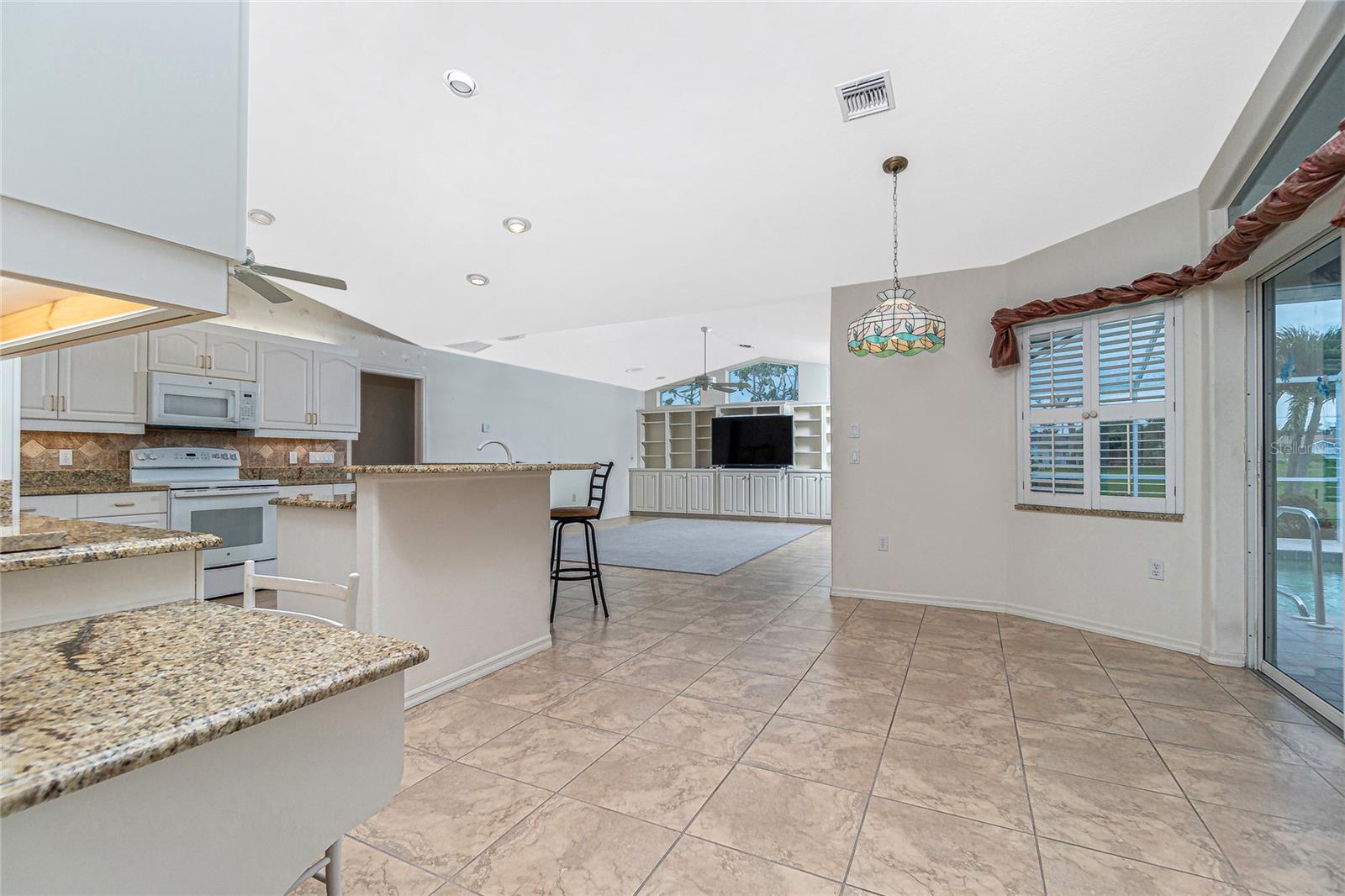 The fully updated and open kitchen includes recessed lighting, granite counters, tiled flooring, newer appliances, built-in desk, and a breakfast nook with sliding doors to the lanai.