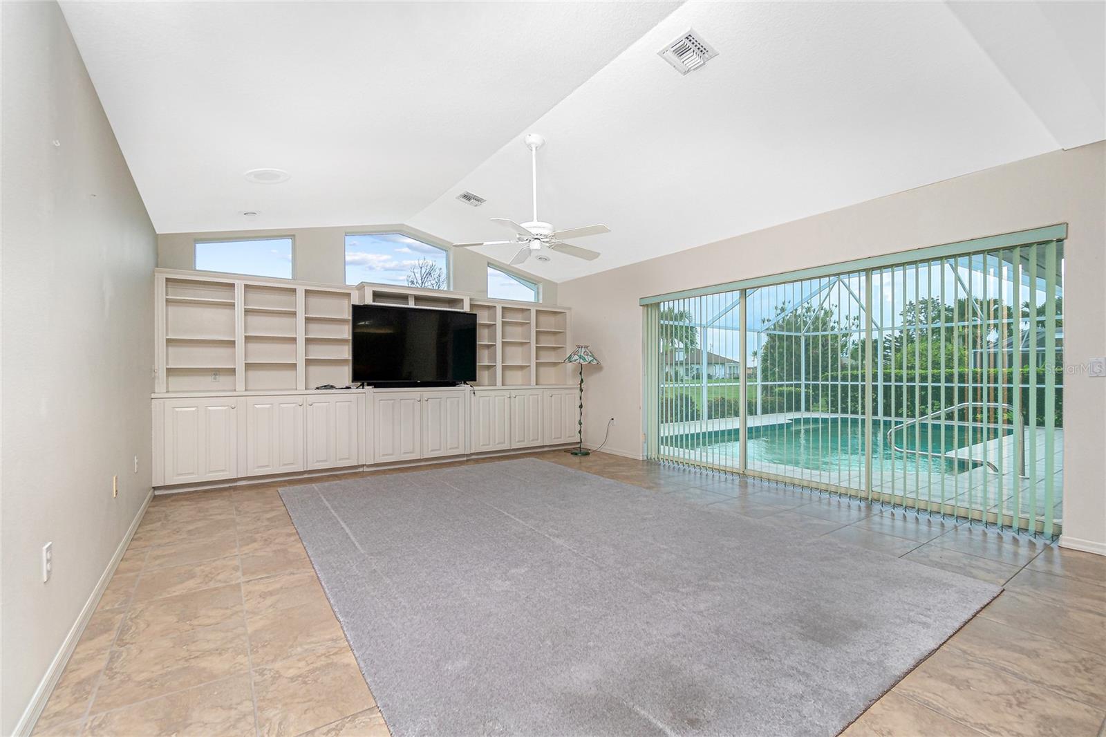 The family room is just off the kitchen and has a cathedral ceiling, tiled flooring, pocket sliding doors to the lanai and built-in cabinetry and open bookcases.