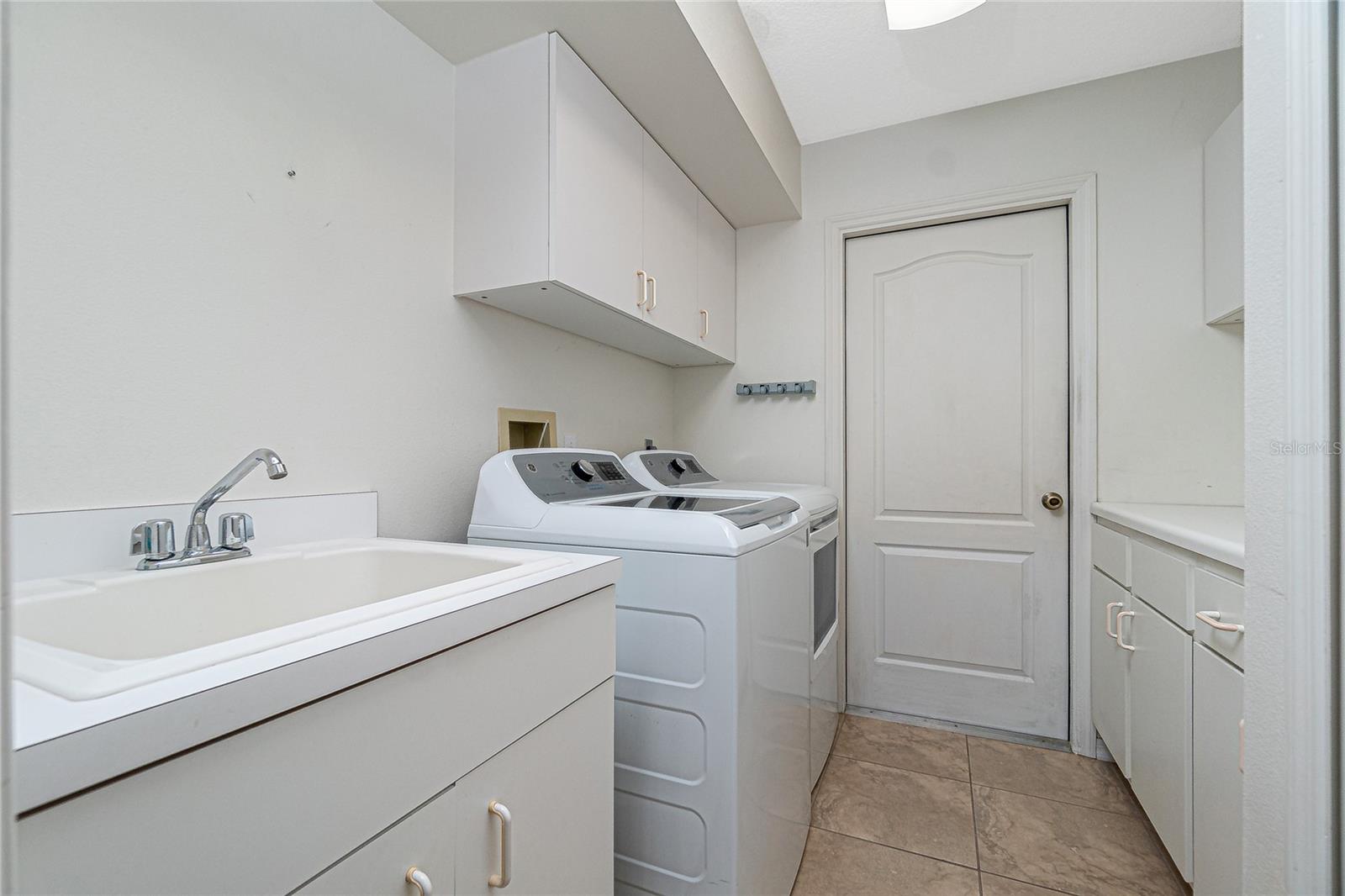 The inside laundry room has built-in upper and lower cabinets, tiled flooring, GE washer & dryer (2020) and utility sink.