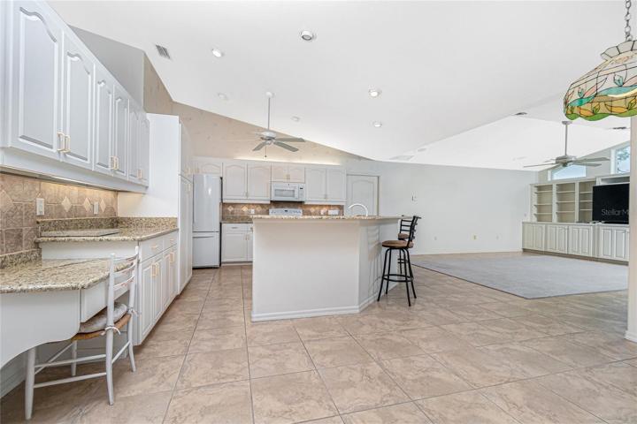 The kitchen has white raised face cabinetry, tiled backsplash, plenty of granite worksurfaces, a panty, plus an island with a convenient breakfast bar.