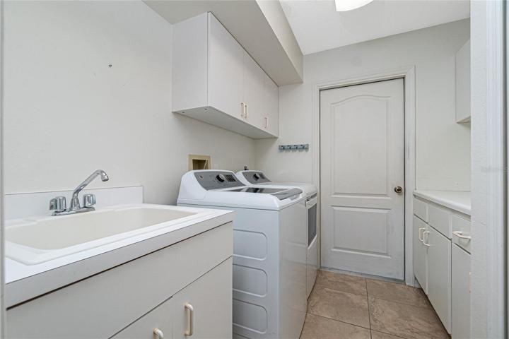 The inside laundry room has built-in upper and lower cabinets, tiled flooring, GE washer & dryer (2020) and utility sink.