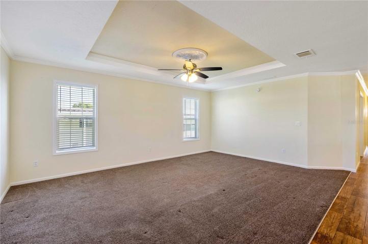 Living room has ceiling fan, tray ceiling, and carpeting.