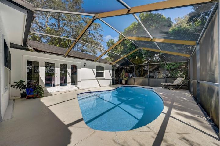 Enjoy entertaining your guests around the screened-in pool & covered patio area.  Looking toward wall of windows and French doors in dinning room and primary bedroom window.
