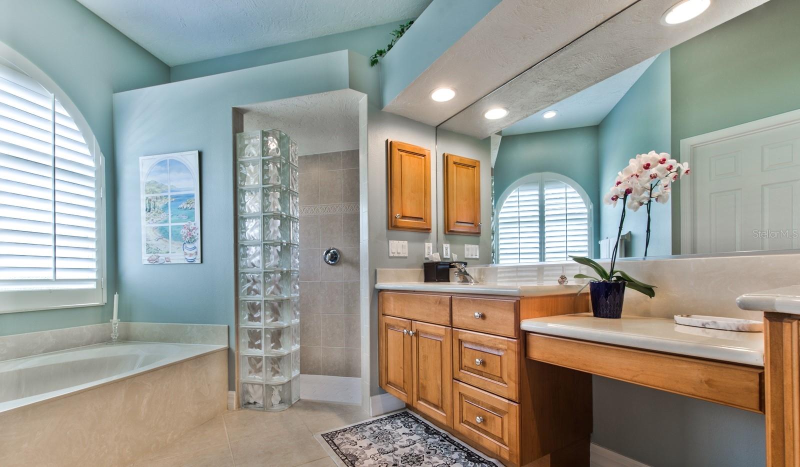The spa-like bath of the owner's suite features a large soaking tub and a spacious walk-in shower framed with a beautiful glass block accent.