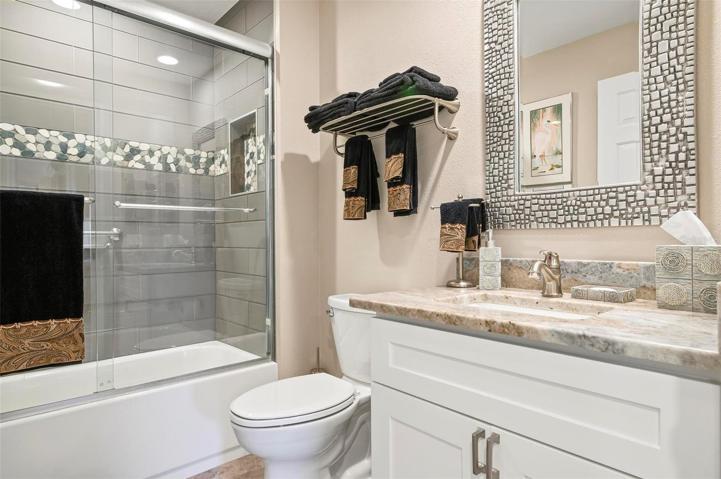 Guest bath with white Shaker cabinets, granite counters, glass enclosed tub