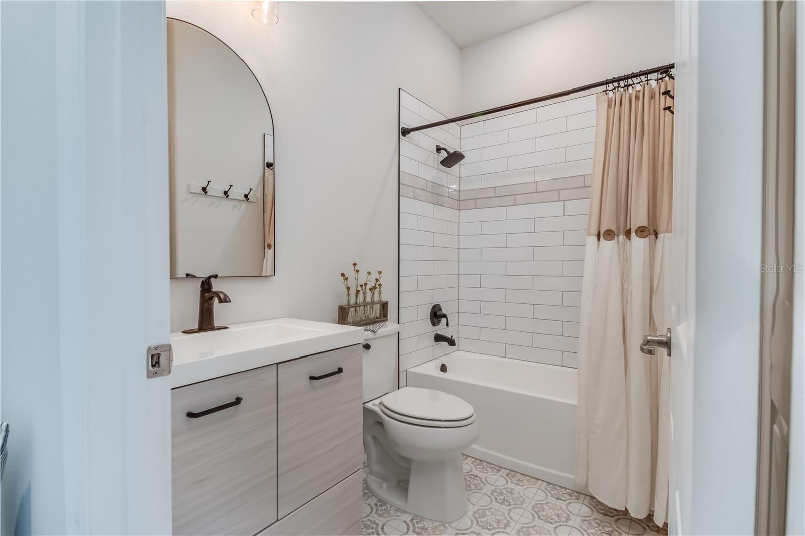 Newly updated guest bathroom with custom tile tub surround, pattern floor tile, new vanity, light fixture, mirror and all new black faucets and hardware.