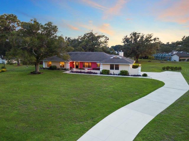 Aerial view of the front Elevation featuring an extended front patio, custom landscape lighting, and large driveway with a extended parking pad all on a spacious 1 acre lot