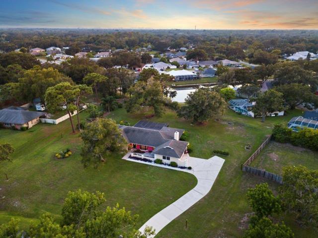 Aerial view of the front Elevation featuring an extended front patio, custom landscape lighting, and large driveway with a extended parking pad all on a spacious 1 acre lot