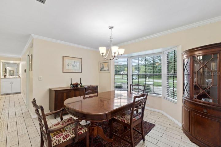 Spacious formal dining room featuring porcelain plank tile, crown molding, and a large bay window.