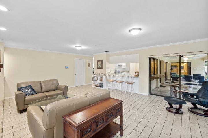 Huge 16'x23' living room with a wood burning fireplace, wet bar, porcelain plank flooring, and crown molding.