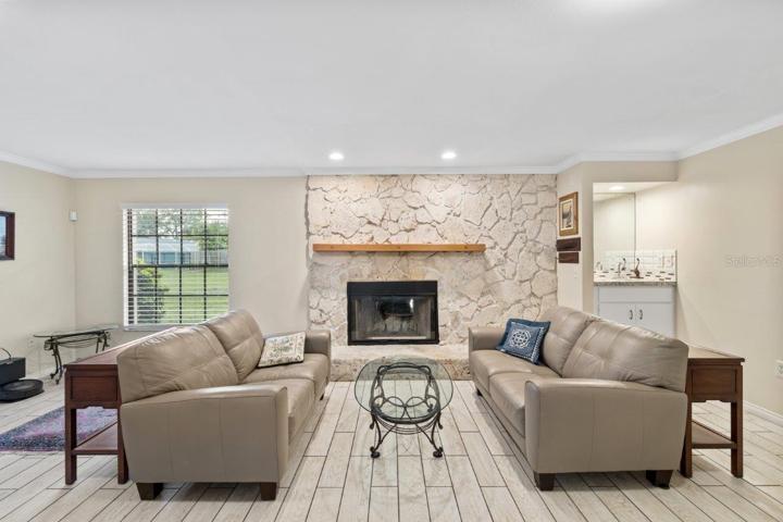 Huge 16'x23' living room with a wood burning fireplace, wet bar, porcelain plank flooring, and crown molding.