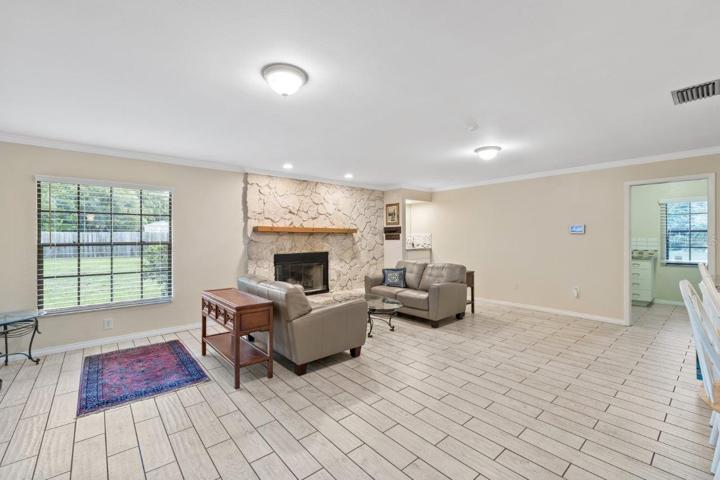 Huge 16'x23' living room with a wood burning fireplace, wet bar, porcelain plank flooring, and crown molding.