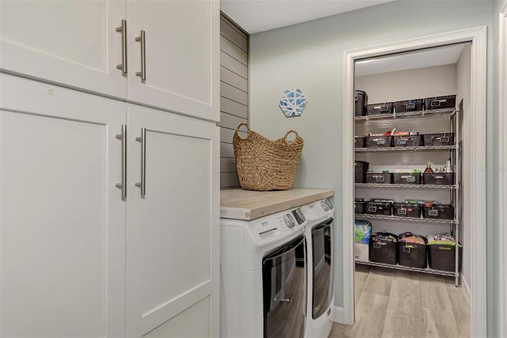 Home has a large laundry room with cabinetry and pull out drawers and the walk-in pantry is just beyond.