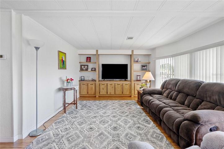 Nice open living room with built-in shelves, ceiling fan, laminate flooring, with orange peel texture on painted walls.