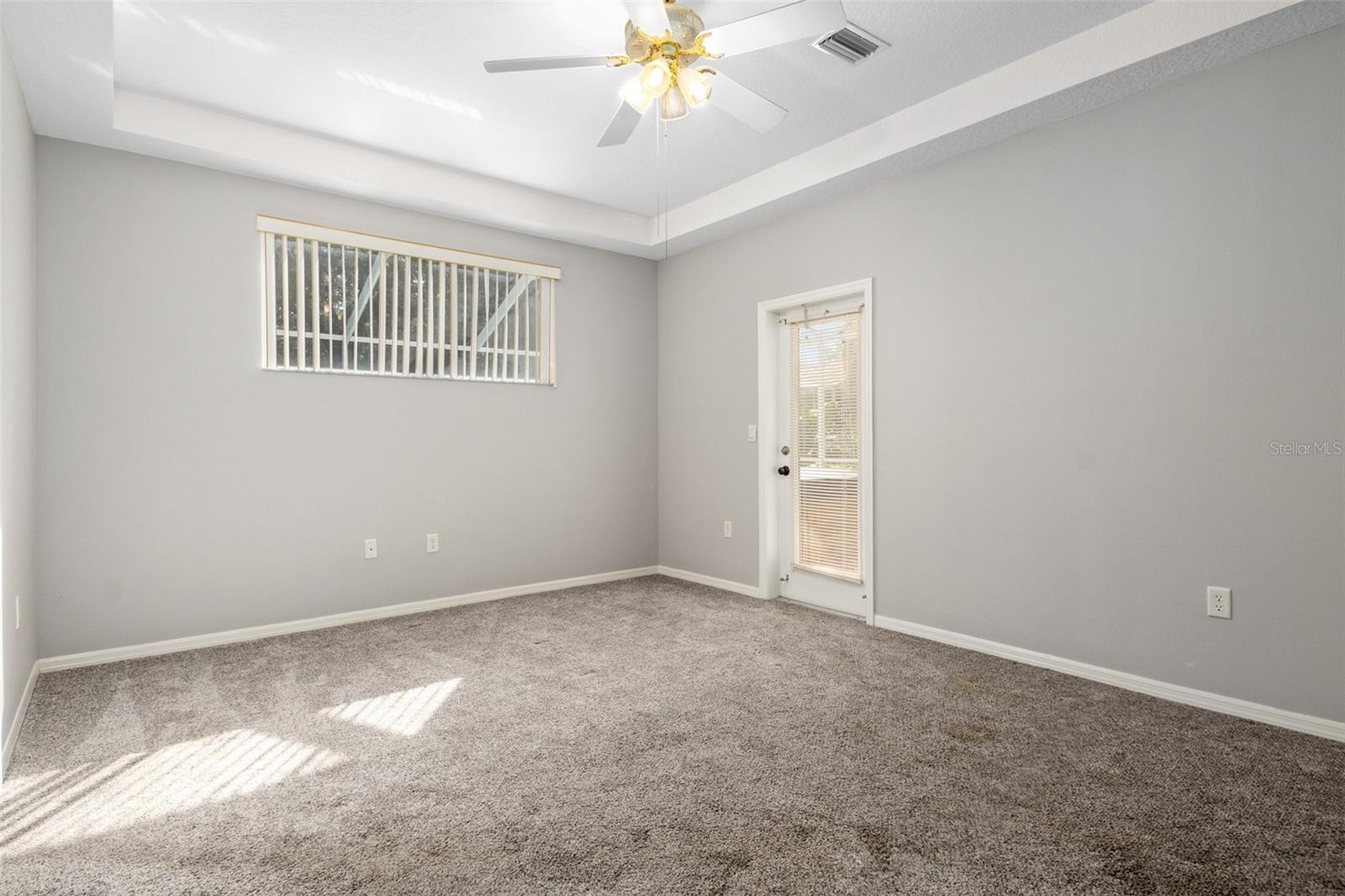 The master bedroom features a tray ceiling, transom window to let light in but still allow for furniture placement underneath, a door to the lanai, and newer carpet.